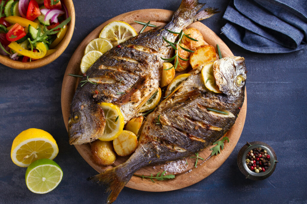 grilled fish with roasted potatoes, lemon and rosemary on wooden tray.