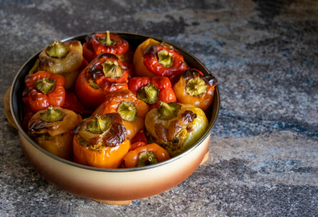 cooked stuffed peppers minced meat baked in oven, paprika with crust under caps in round baking dish on wooden stand. stone work kitchen surface. healthy dish recipe. meat with vegetables. copy space.