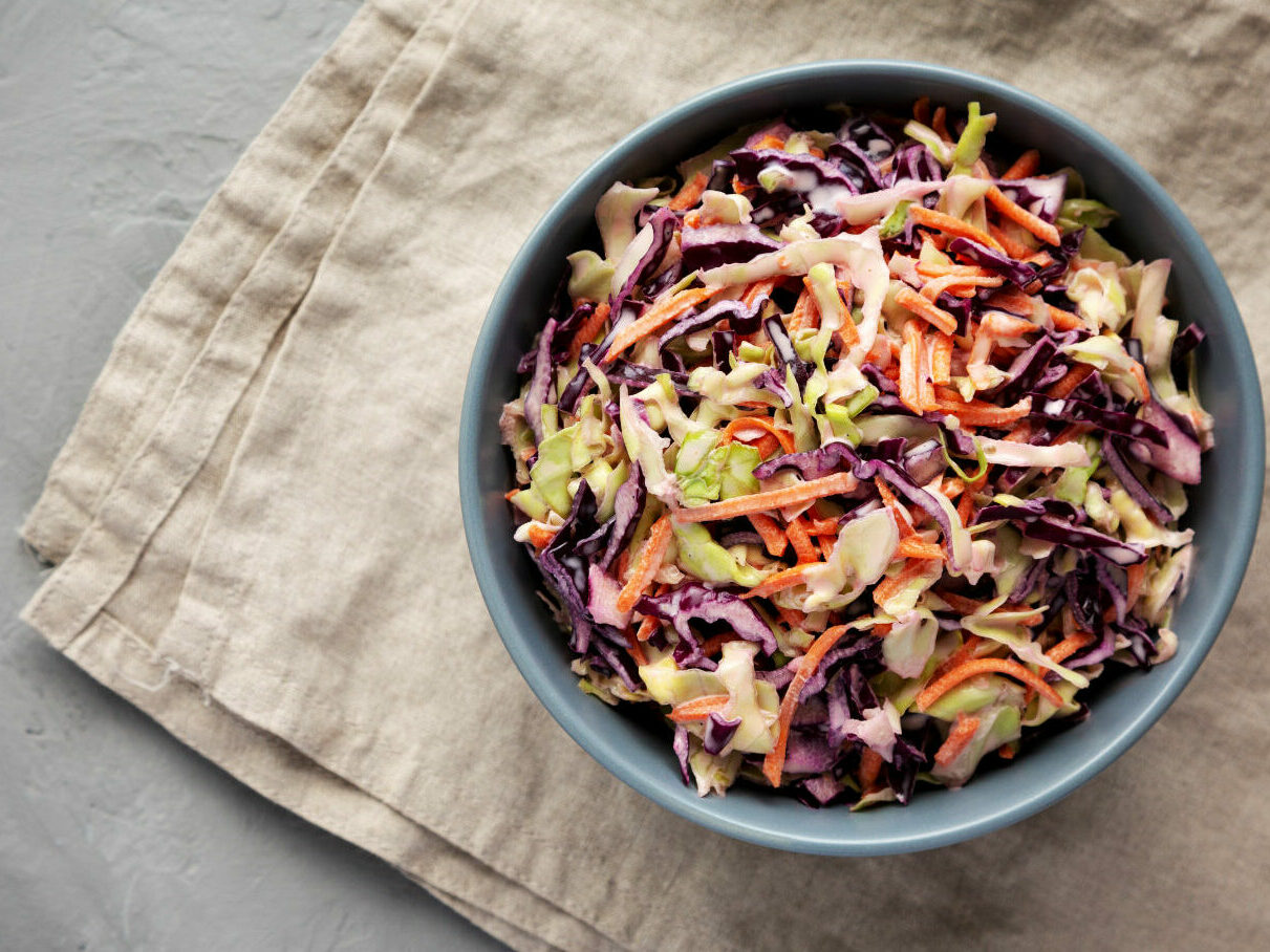 homemade coleslaw with cabbage and carrots in a bowl, top view.
